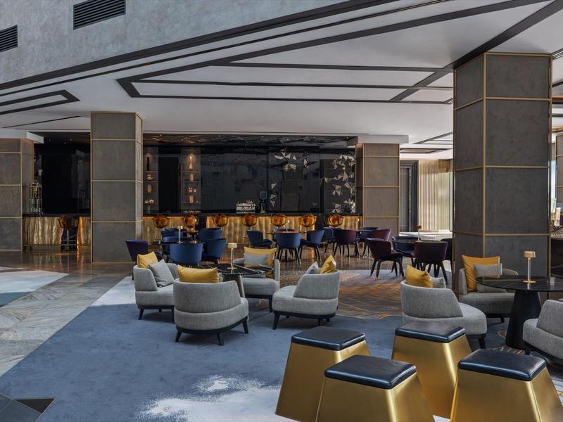 Moderne Hotellobby mit grauen Sesseln, blauen Teppichen und dunklen Holzmöbeln.