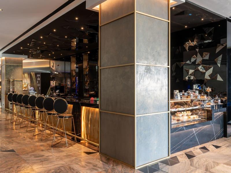 Elegante Hotelbar mit schwarzer Theke, goldenen Akzenten und bequemen Barhockern in modernem Design.