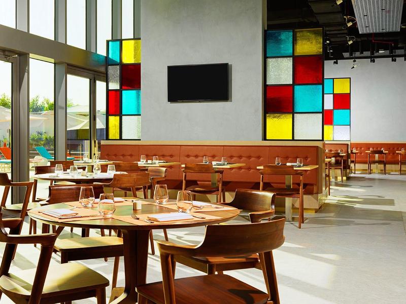 Modernes Café mit Holztischen, farbigen Glasfenstern und viel natürlichem Licht.