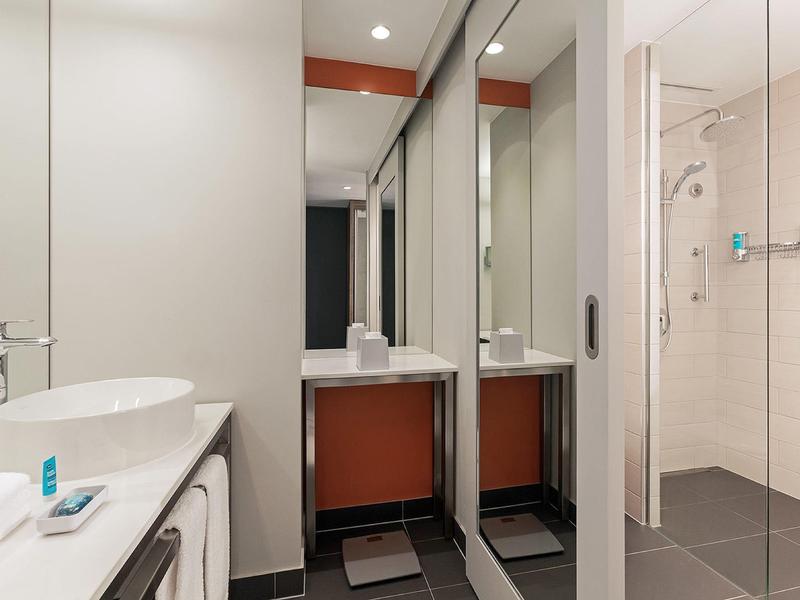 Moderner Badbereich mit weißer Wand, großem Spiegel und offener Dusche mit Duschkopf und Halterungen.