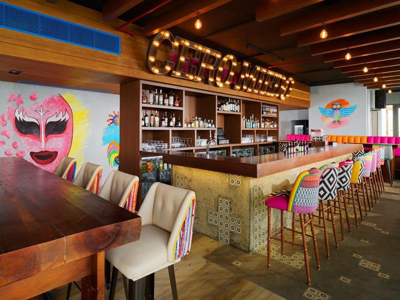 Moderner Barraum mit farbenfrohen Wandbildern, Holzdecke und Sitzplätzen an Theke und Tischen.