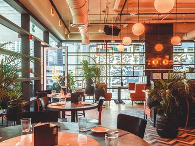 Modern hotel restaurant with large windows, plants, and stylish tables and chairs.