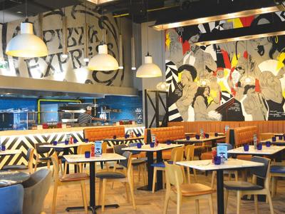 Interior of a modern restaurant with colorful wall art and light wooden furniture.