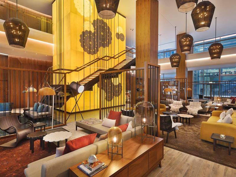 Espace lounge d'hôtel moderne avec accents jaunes et lampes suspendues.