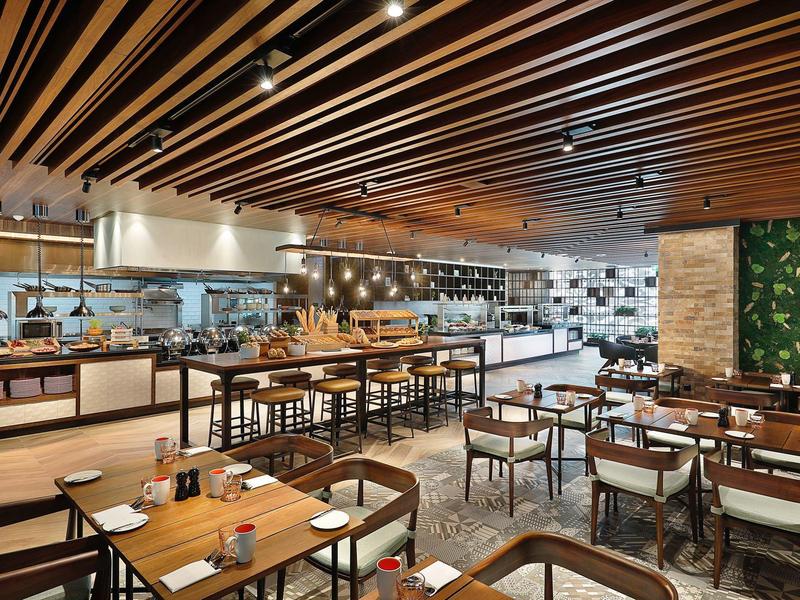 Restaurant moderne avec mobilier en bois, cuisine ouverte et plafond en bois décoratif.