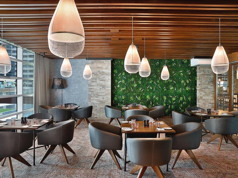 Restaurant d'hôtel moderne avec des fauteuils en cuir, un mur végétal vert et des luminaires suspendus.