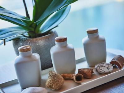 Drie witte flessen en natuurlijke badartikelen op een dienblad naast een plant bij het zwembad.