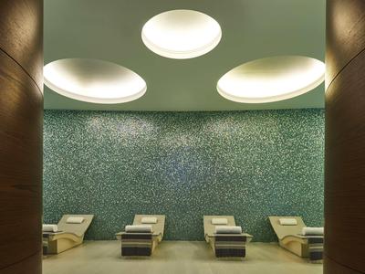 Moderne ontspanningsruimte met ligstoelen voor een groene mozaïekmuur en ronde plafondlampen.