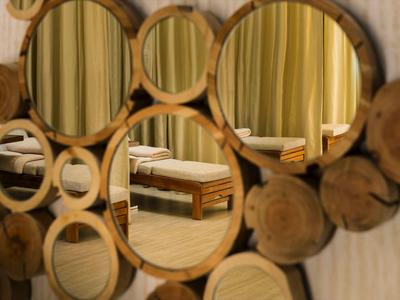 Ronde houten spiegel met meerdere kleinere en grotere spiegels, weerspiegelt een hotelbed en gordijnen.