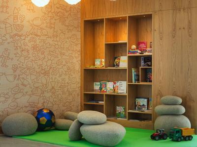 Gezellig speelgedeelte voor kinderen met zachte kussens, voetbal en houten planken vol boeken en speelgoed.