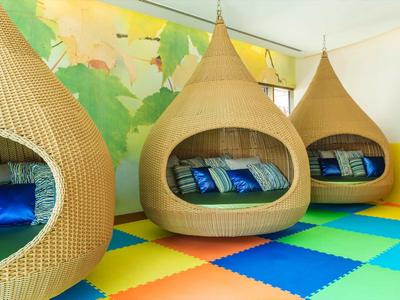 Drie ronde rieten hangstoelen met kleurrijke kussens in een kamer met een felgekleurde speelmatvloer.