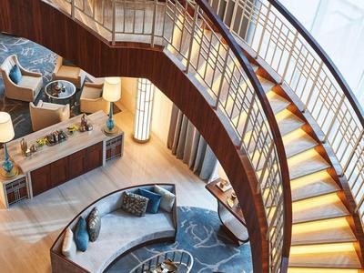 Gebogen houten trap met verlichting boven zithoek in modern hotelinterieur.