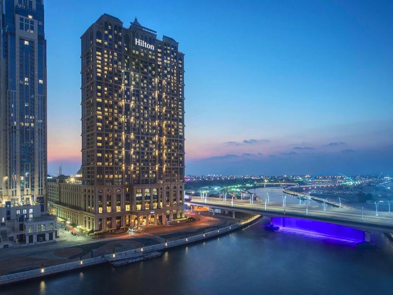 Hoog gebouw aan de rivier bij schemering met verlichte brug en stadszicht