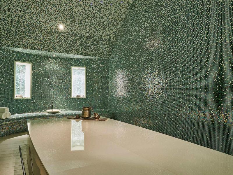 Moderne spa ruimte met groot bad en groene mozaïektegelwanden.