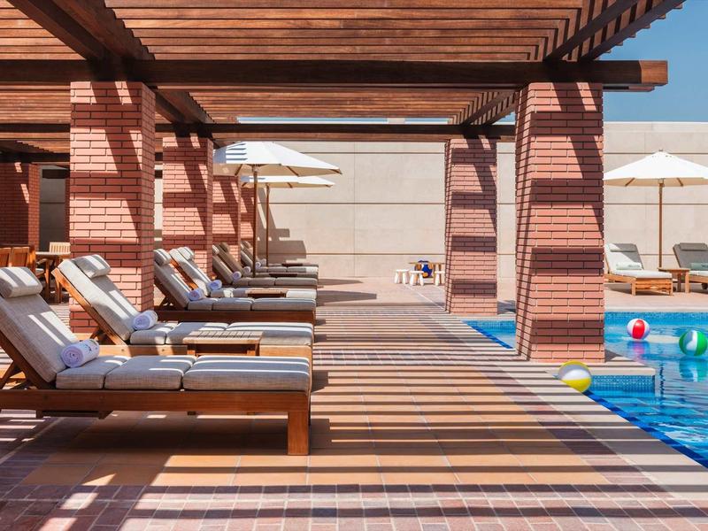 Zwembadgedeelte met ligstoelen onder een houten pergola, parasols en kleurrijke ballen in het water.