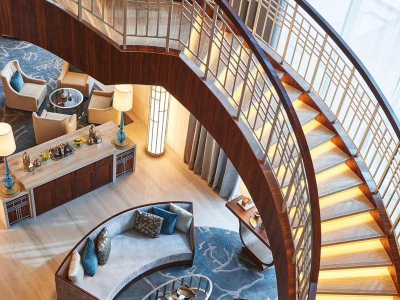 Gebogen houten trap met verlichting boven zithoek in modern hotelinterieur.