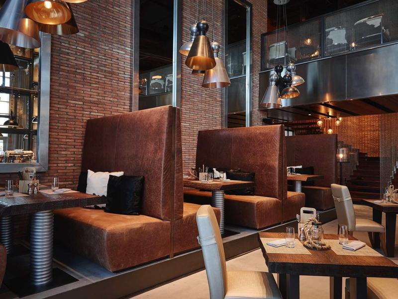 Gezellig restaurant met bruine leren banken en warme koperen lampen.