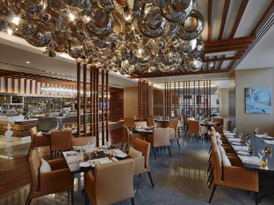 Moderner Gastraum mit braunen Ledersesseln, weißen Tischen und einer Decke aus vielen Metallkugeln.