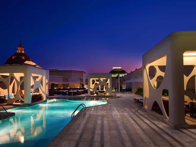 Zona de piscina moderna con pabellones iluminados y áreas para sentarse por la noche