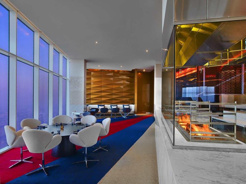 Area lounge moderna dell'hotel con grandi finestre, sedie bianche e accogliente camino.