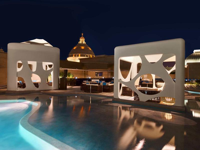 Area piscina illuminata con architettura moderna e edificio a cupola sullo sfondo di notte.