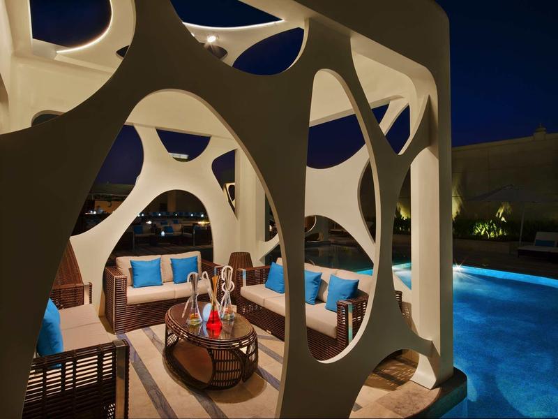 Lounge accogliente con mobili bianchi moderni e piscina blu sullo sfondo di notte.