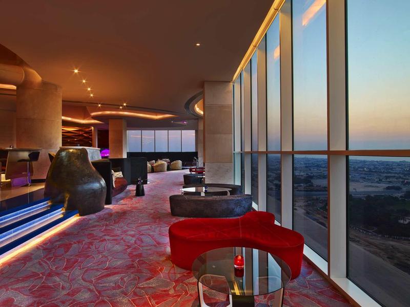 Lounge di hotel lussuoso con poltrone rosse e ampie finestre panoramiche al tramonto.