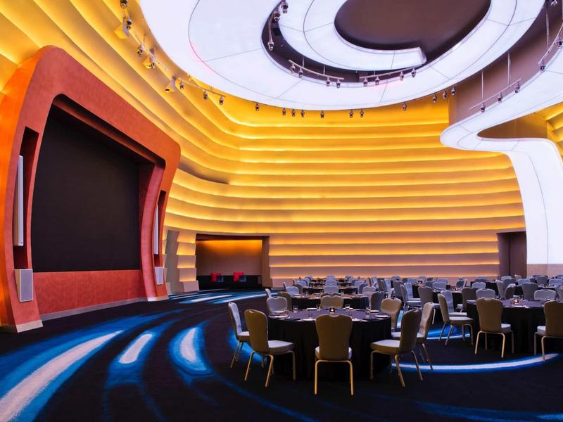 Sala eventi moderna con pareti curve e file di sedie di fronte a un grande palco.