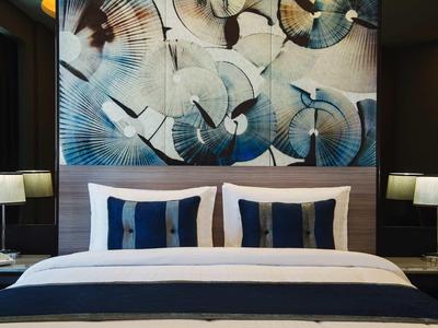 Habitación de hotel moderna con cama doble, cojines elegantes y arte abstracto en la pared detrás del cabecero.