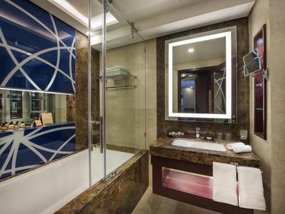 Baño de hotel moderno con espejo iluminado, ducha de vidrio y lavabo de mármol.