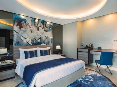 Habitación de hotel moderna con cama grande, ropa de cama azul y blanca, y decoración de pared elegante.