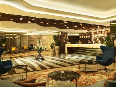 Área moderna de lobby de hotel con recepción, asientos y elementos de iluminación cálida.
