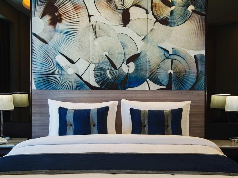 Habitación de hotel moderna con cama doble, cojines elegantes y arte abstracto en la pared detrás del cabecero.