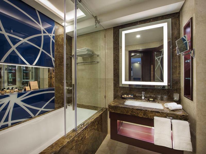 Baño de hotel moderno con espejo iluminado, ducha de vidrio y lavabo de mármol.