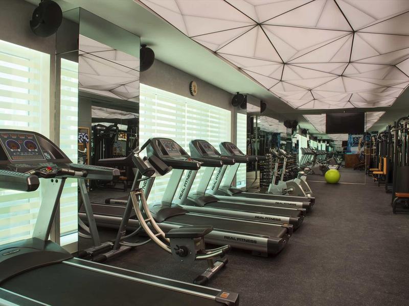 Gimnasio moderno con cintas de correr, espejos y luz natural brillante a través de grandes ventanas.