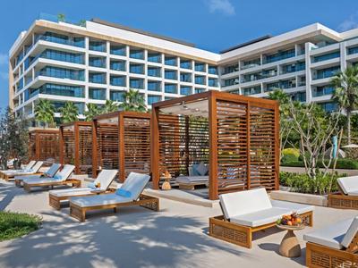 Moderní hotelová bazénová oblast s dřevěnými pergolami a lehátky pod modrou oblohou