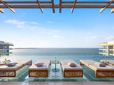 Lettini di lusso vicino alla piscina su un pontile in legno con vista sul mare e cielo limpido in un resort.
