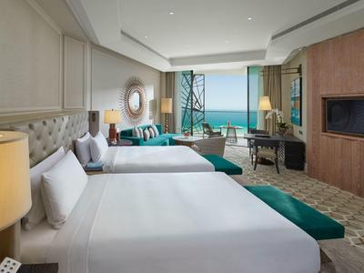 Moderně zařízený hotelový pokoj se dvěma postelemi a výhledem na moře přes velká okna.