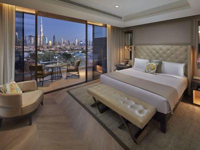 Moderní hotelový pokoj s velkou postelí a balkonem s nočním výhledem na město.