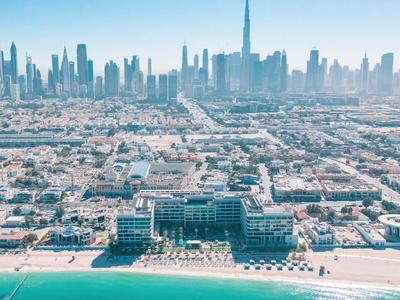 Plážové letovisko s moderními budovami před městským panoramatem a modrou oblohou