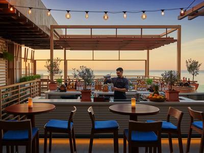 Ristorante sul tetto con vista sul mare al tramonto, tavoli e sedie in primo piano.