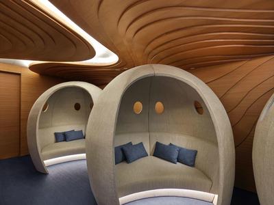 Pohodlné kulaté lounge niky s modrými polštáři v moderním prostoru se zakřivenými dřevěnými stěnami.