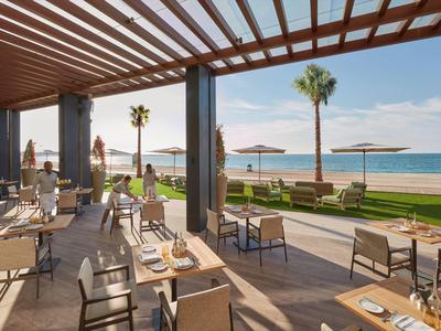 Otevřená terasa restaurace s výhledem na pláž a moře za slunečného počasí.