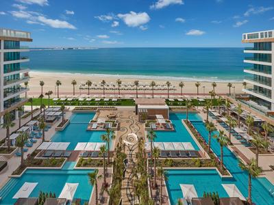 Complesso alberghiero moderno con più piscine e accesso diretto alla spiaggia sabbiosa e al mare.