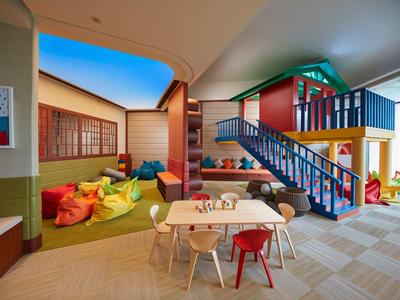 Barevná dětská herna se stoly, židlemi a domečkem uvnitř hotelu.