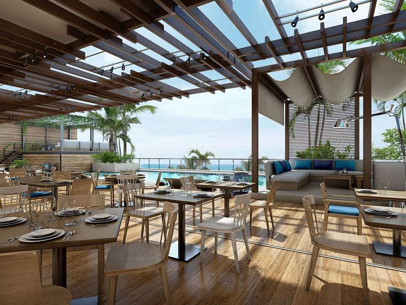 Světlá střešní terasa s dřevěnou podlahou, jídelními prostory a výhledem na moře za jasné oblohy.