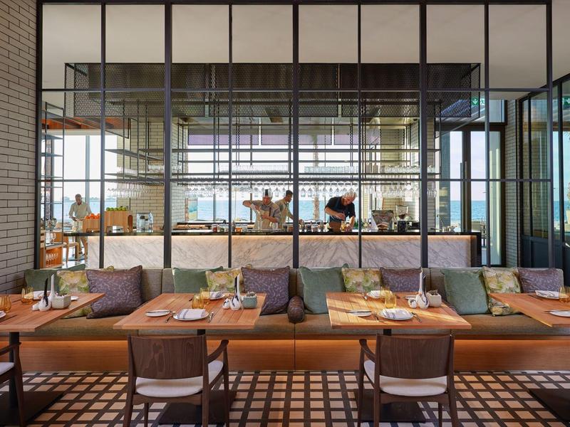 Moderní restaurace s posezením a velkou prosklenou stěnou s výhledem do kuchyně.