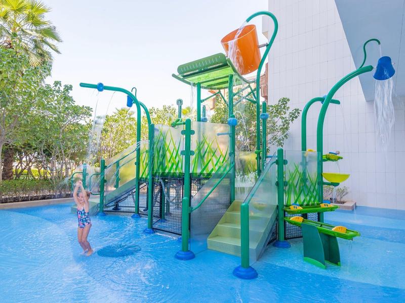 Dětská herní zóna s vodními prvky a skluzavkami v mělkém venkovním bazénu