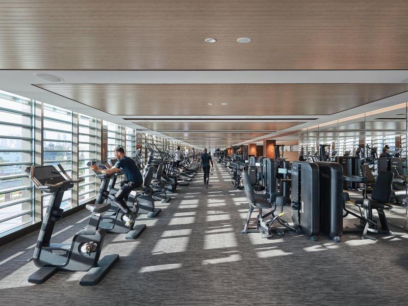 Prosvětlené fitness centrum s moderními stroji a velkými okny propouštějícími denní světlo.