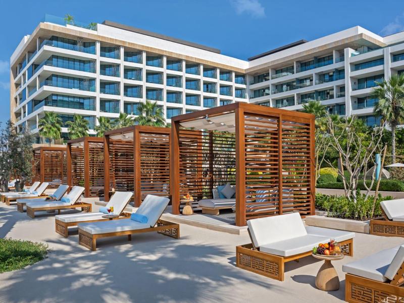 Moderní hotelová bazénová oblast s dřevěnými pergolami a lehátky pod modrou oblohou